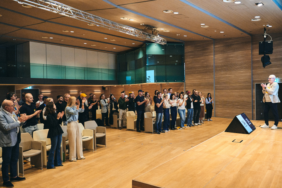 Atlantis Headwear hosts its “30 Hats Later” global meeting in Italy, with distributor partners standing and applauding during a presentation.