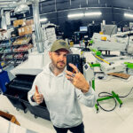 Lee Stuart takes a mirror selfie inside Rogue Lab’s screen printing shop, showcasing professional apparel decoration equipment and workspace.