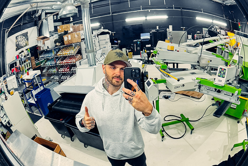 Lee Stuart takes a mirror selfie inside Rogue Lab’s screen printing shop, showcasing professional apparel decoration equipment and workspace.