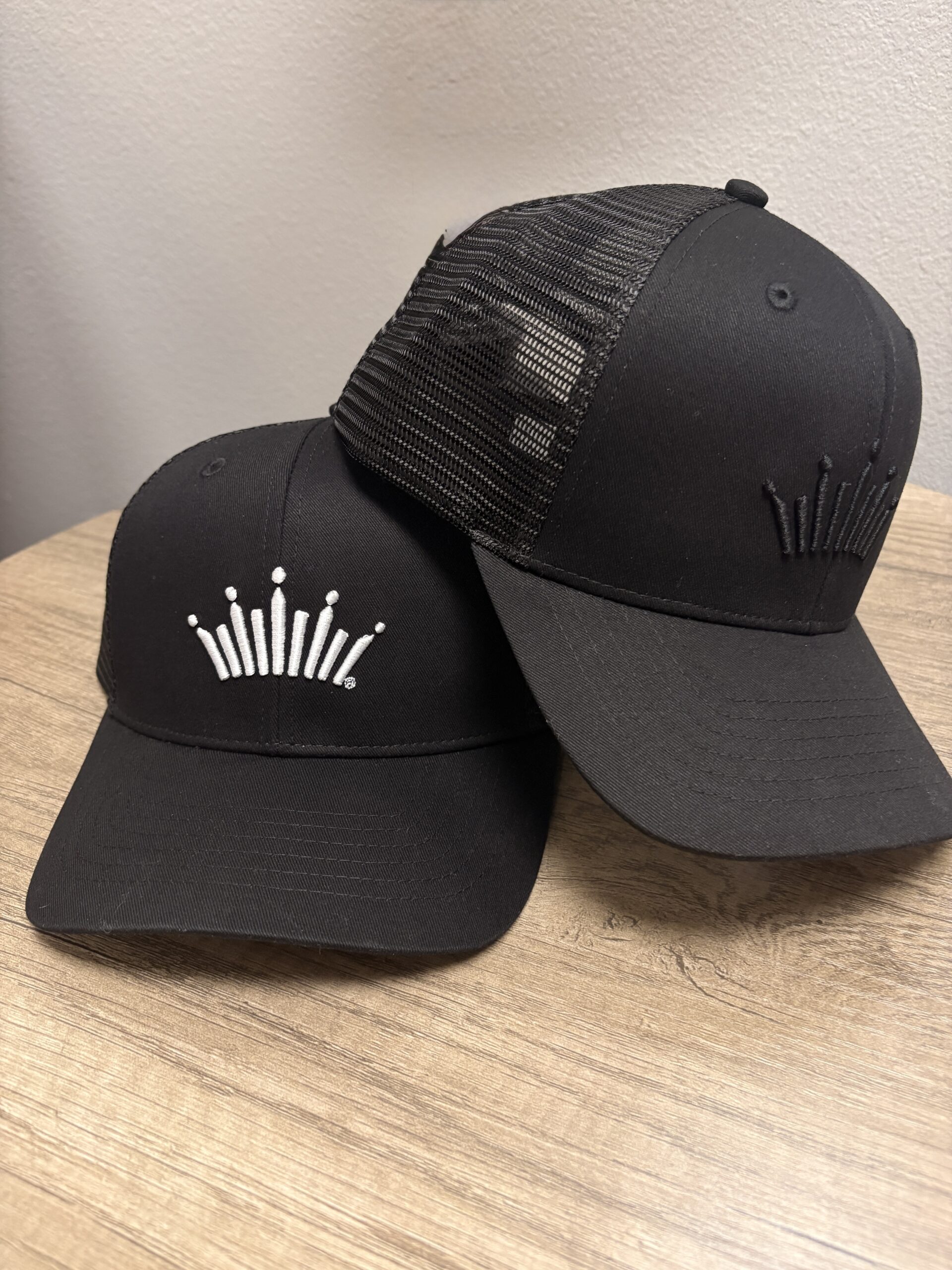 Infinity Product Group branded black headwear samples shown as part of the company’s new Anheuser-Busch licensing partnership for premium apparel and accessory collections.