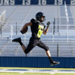 High school football player sprinting across a field wearing an A4 performance football uniform featuring moisture-wicking athletic fabric and custom team graphics.