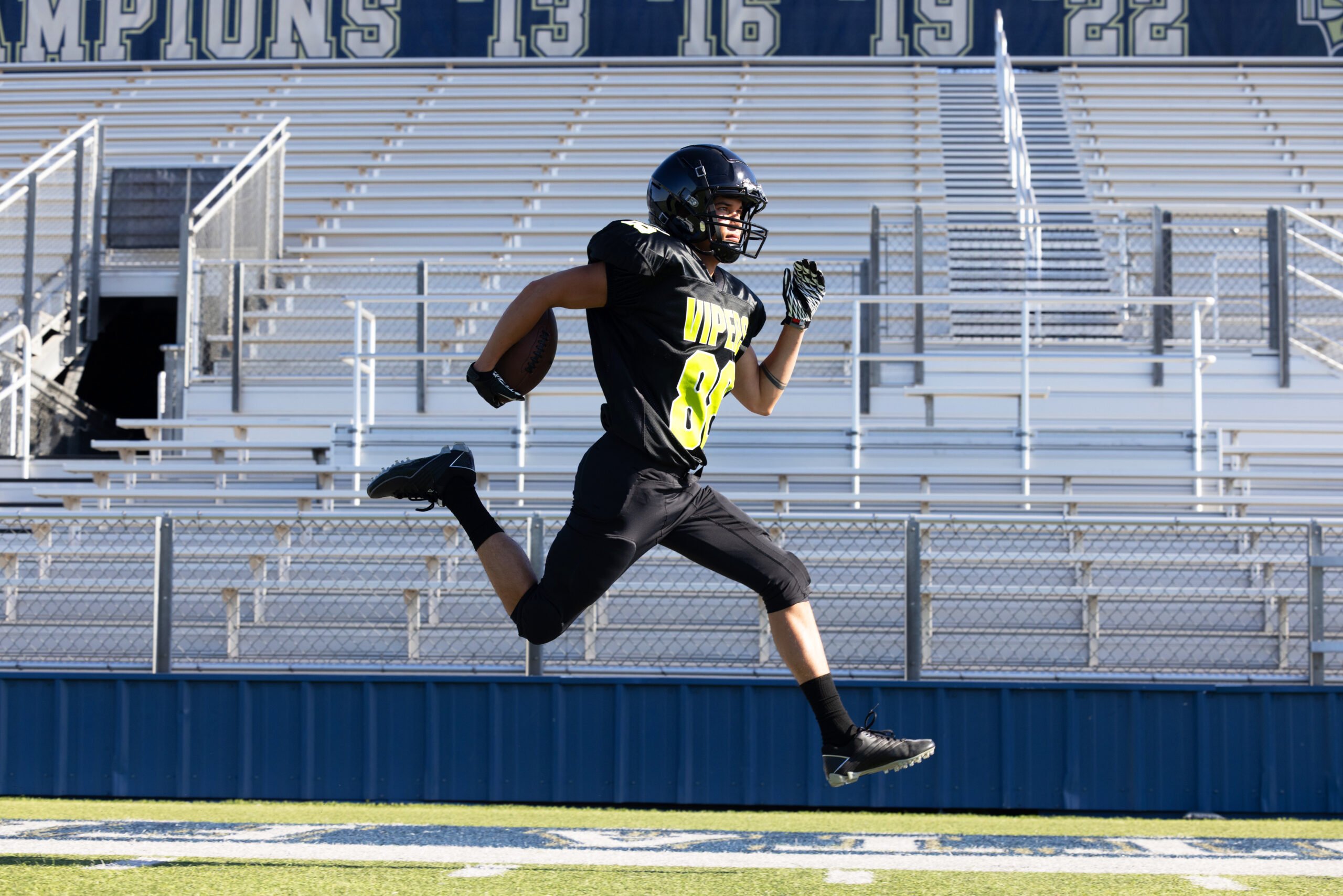 High school football player sprinting across a field wearing an A4 performance football uniform featuring moisture-wicking athletic fabric and custom team graphics.