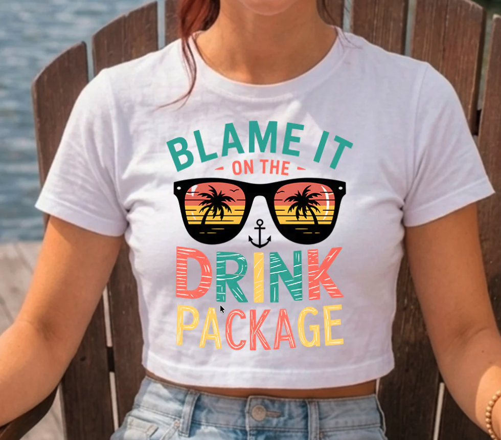 Crystal DTF Summer 2026 ready-to-press transfer featuring the phrase “Blame It on the Drink Package” with colorful retro typography, tropical sunglasses and palm trees displayed on a white cropped T-shirt, highlighting the company’s vibrant DTF printing capabilities for custom apparel decorators.