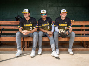 Baseball players seated in a dugout wearing custom Momentec team uniforms with performance jerseys, athletic pants, and coordinated team branding.
