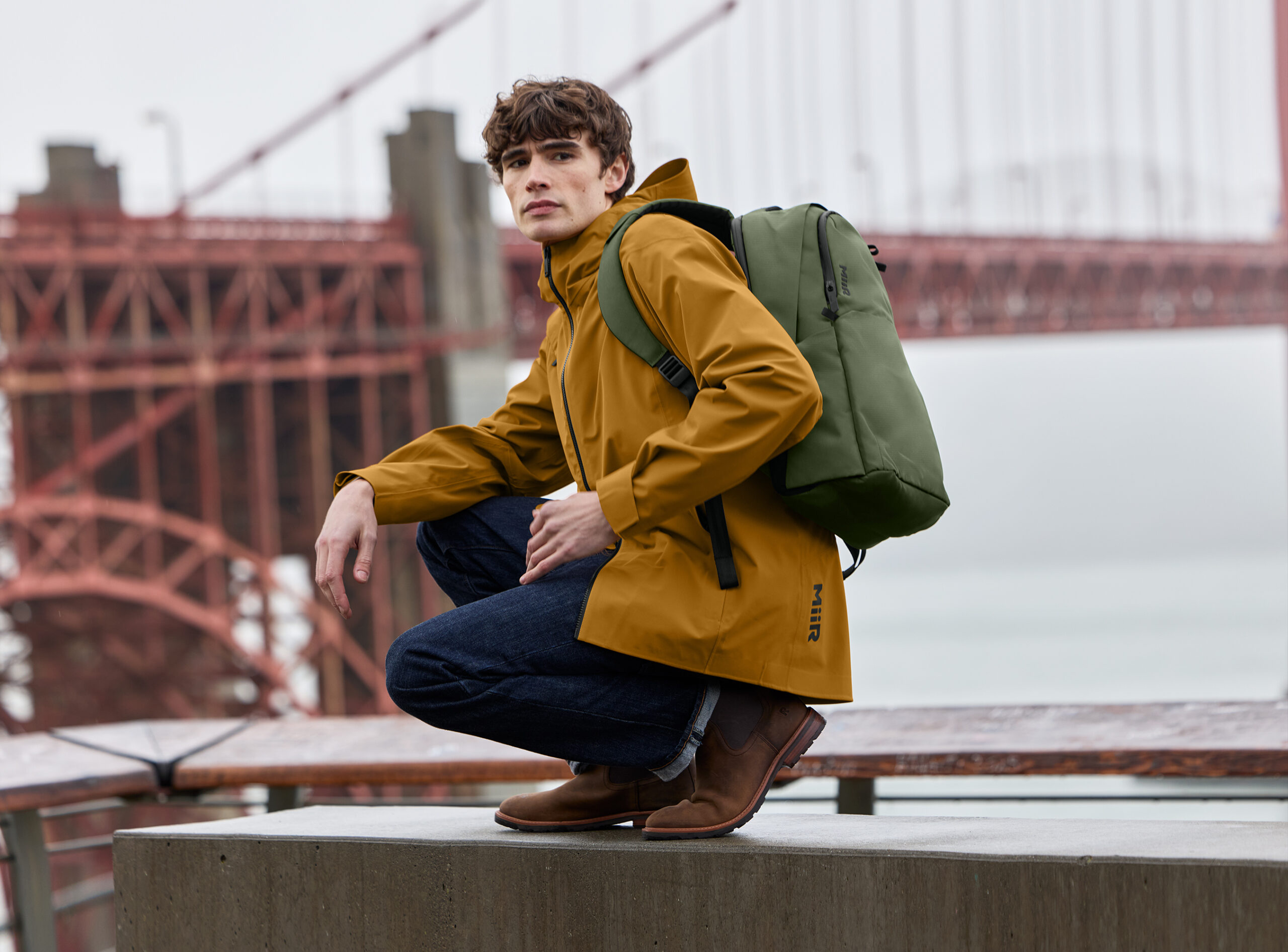 Model wearing MiiR outdoor apparel featuring a Forest Moss jacket and Amber Haze layering piece from SanMar's 2026 Fall collection.