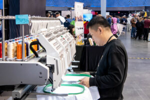 Decorator operating commercial multi-head embroidery machine for apparel production at Impressions Expo 2026 PWP Studio Corporate Event Photographers