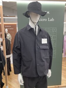 Mannequin wearing a dark technical jacket with oversized pockets and a matching bucket hat at a Toray textile exhibition.